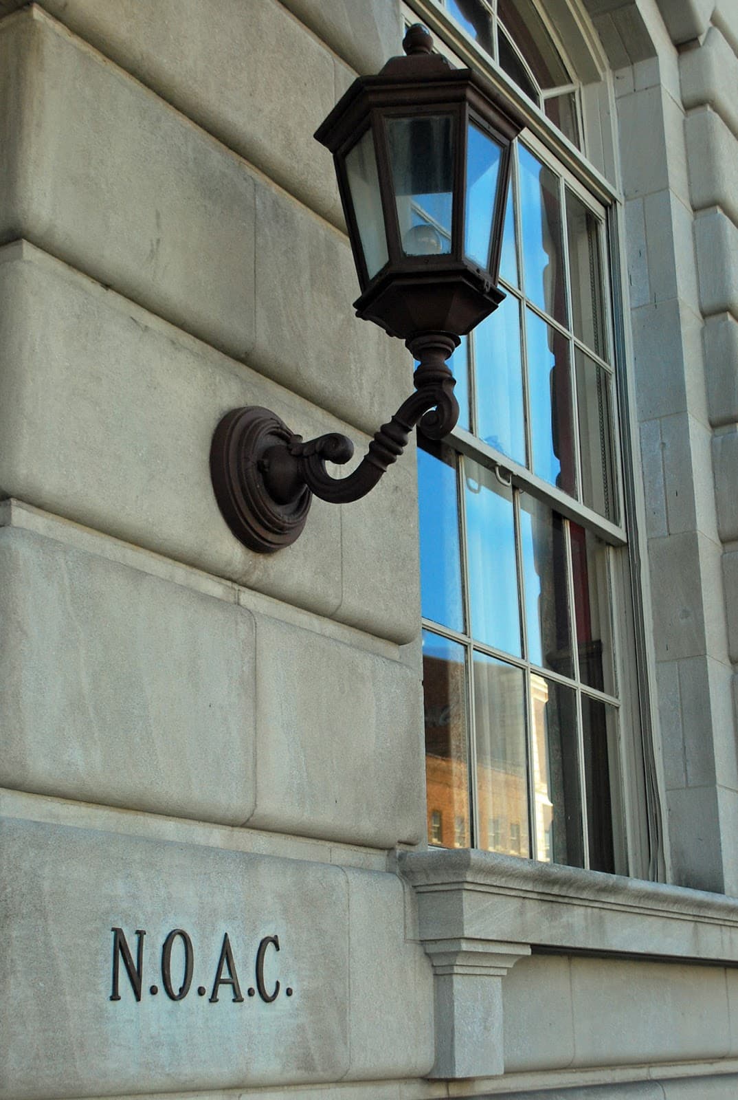 A black lantern is attached to a stone building. The building has "N.O.A.C." carved into the stone below the lantern. 