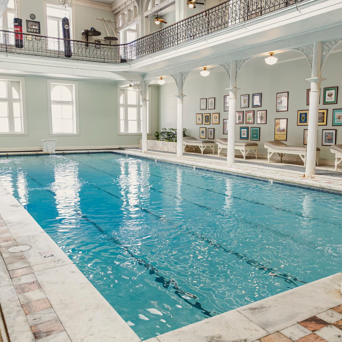 Rectangular swimming pool with lights in between the columns surrounding it. The walls are white and have several frames hanging on them.