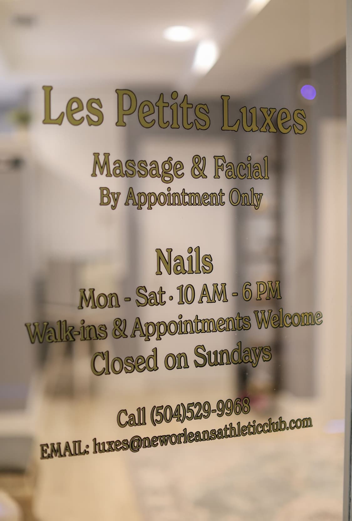 A nail salon has two white pedicure chairs, beige towels, and a black rolling chair in front of the chairs. It has a white shelf with nail polish bottles between the two chairs.