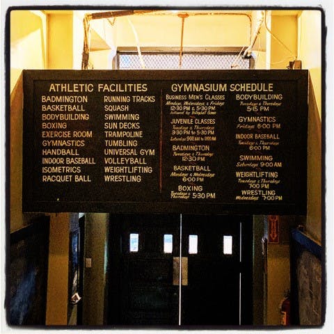 The blackboard sign lists athletic facilities and gymnasium schedules at New Orleans Athletic Club. It is divided into two columns. The left column lists the athletic facilities, and the right column lists the gymnasium schedule.