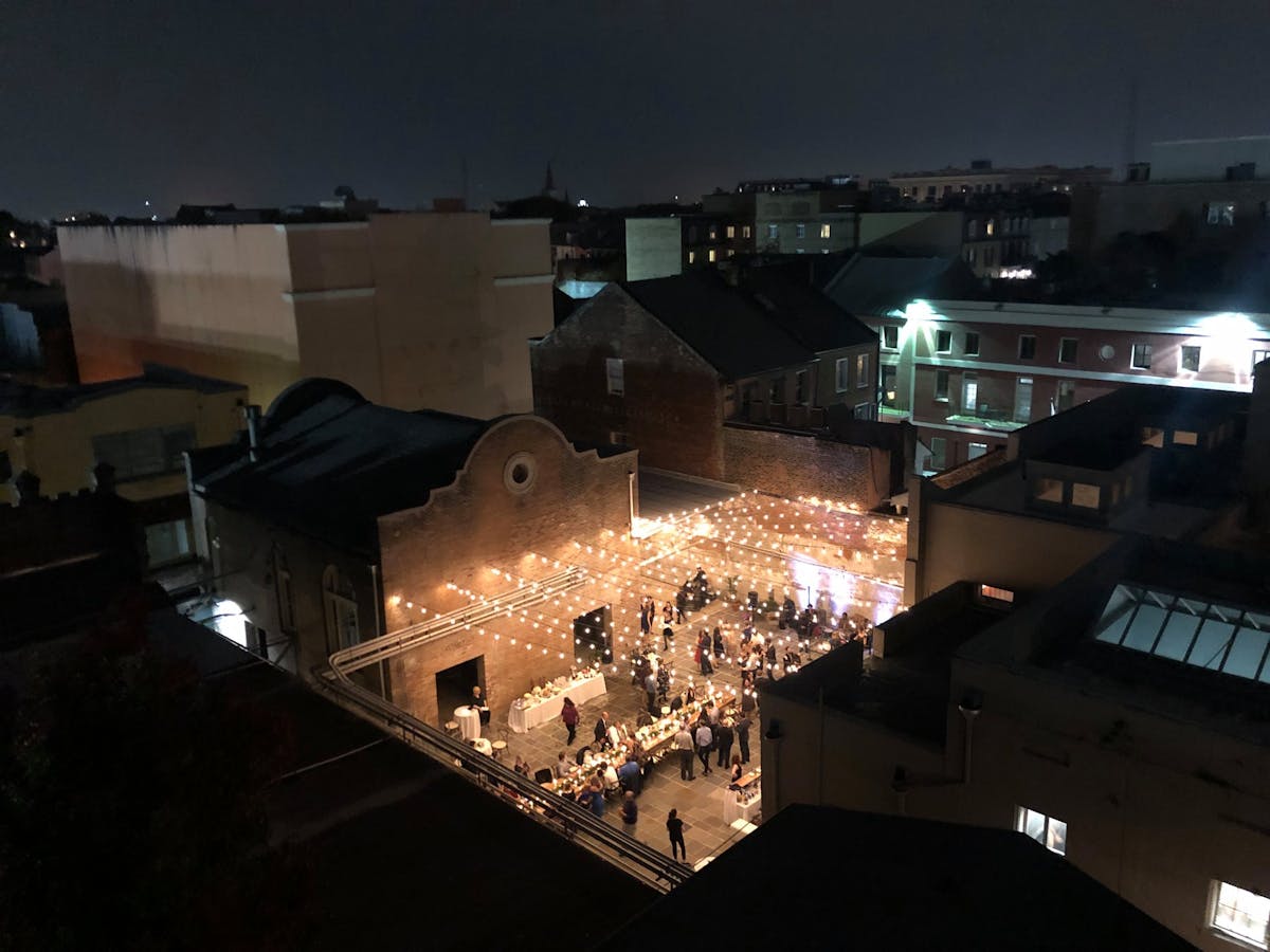 People gather at NOAC’s courtyard at night with string lights hung in a zigzag pattern across the yard. 
