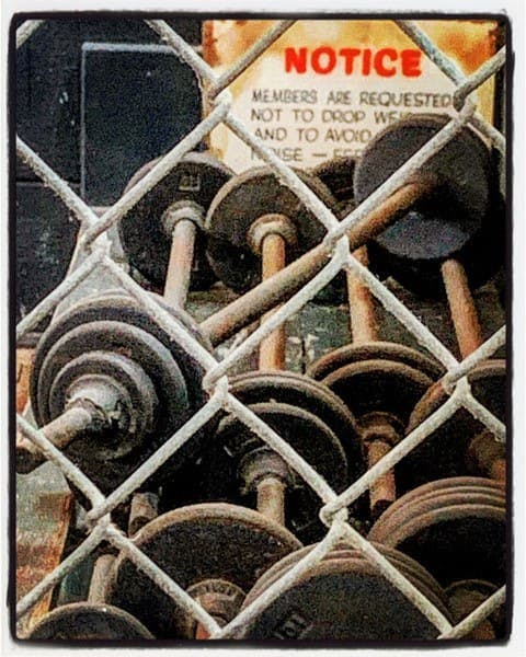 Black weights on a rack inside a cyclone fence. On the background is a NOTICE sign in orange and black text.