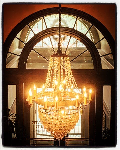 A chandelier is hanging in front of a window. It is made of multiple tiers of crystal beads and has multiple candle-like lights.