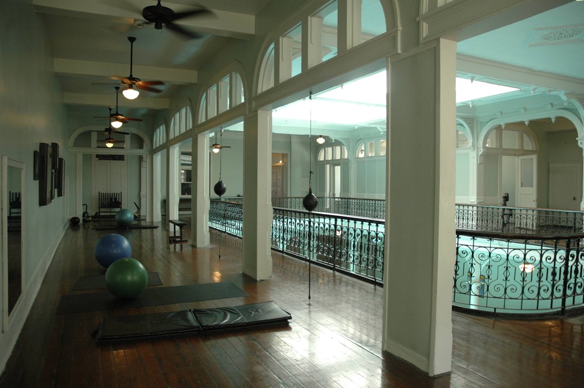 A hallway with white walls, several exercise balls, and yoga mats on the floor. It has a black metal railing in the center.