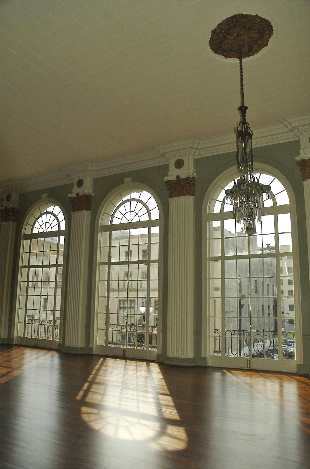 A large room with tall arched windows and a chandelier. It has a high ceiling with a white plaster finish.