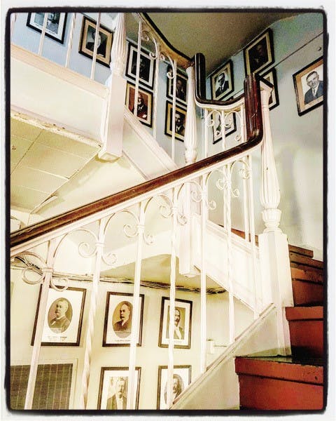 A staircase with reddish brown steps, a white railing, and a wall of framed photos of the presidents of the United States. 