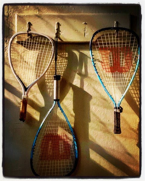 Three tennis racquets are hanging on a white wall. The racquet at the center is hanging upside down.